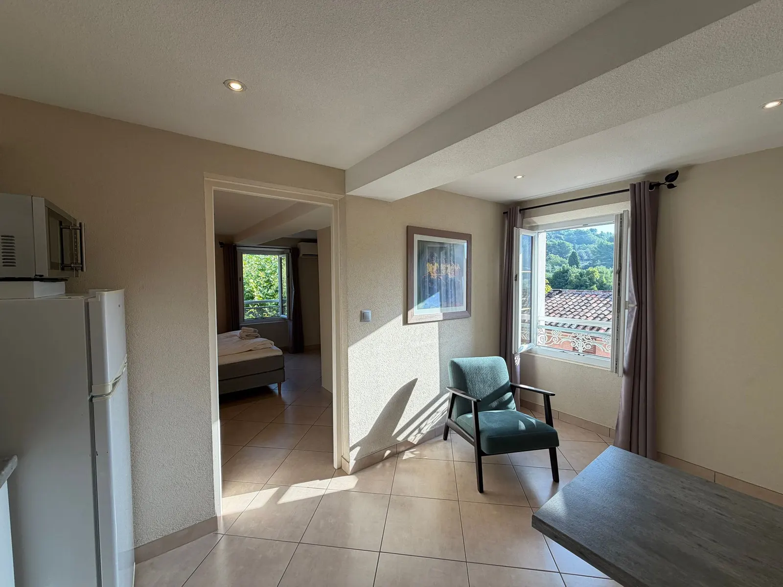 Séjour ouvert du studio avec fauteuil, réfrigérateur et vue sur la chambre